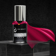 5ml black bottle with silver cap. label reads "Yegi Beauty Ultra Bonding Adhesive For Eyelash Extensions." Bottle is wearing red super hero-like cape to play with "Ultra" aspect of glue.