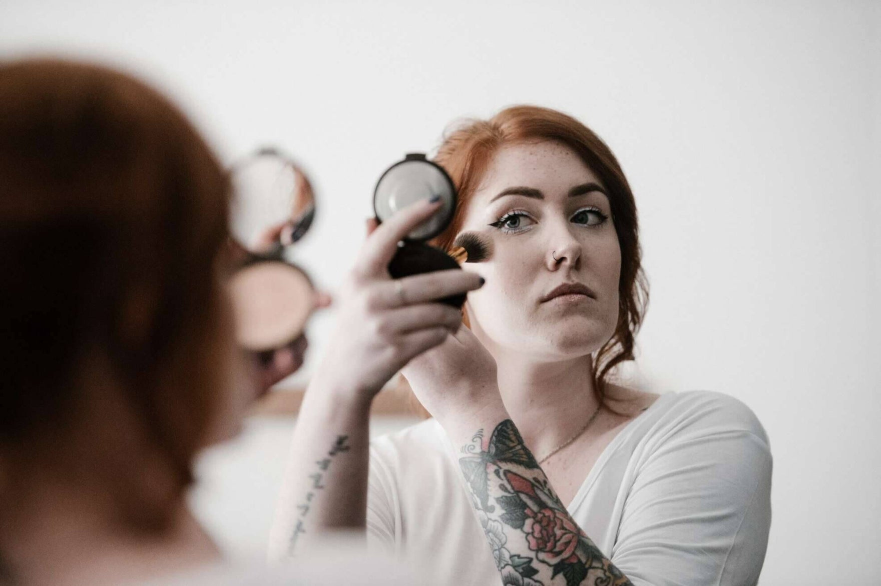 A woman looking in a cosmetic mirror and applying makeup