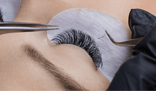 A lash extension technician applying lashes with tweezers