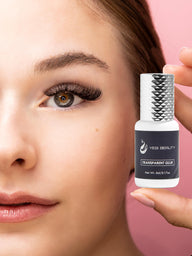 Woman with colored eye and sporting eyelash extensions holding small 5ml white bottle with gray label and silver cap. Label reads "Yegi Beauty Transparent Glue"