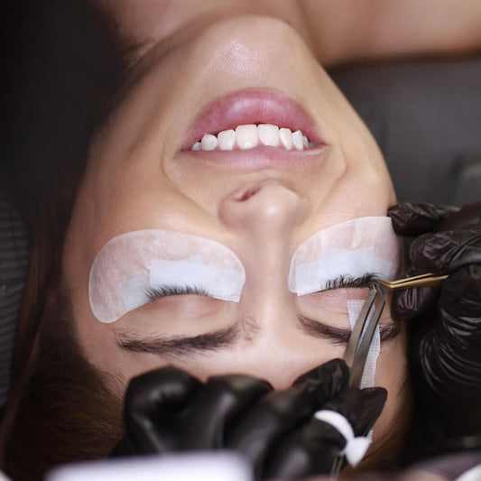 Woman getting eyelash extensions with under eye patches and tape.