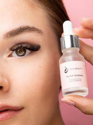 Product bottle held by model with colored eyes and eyelash extensions against pink background. Bottle reads "Super Bonder" 