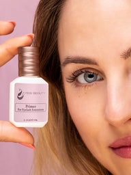 15ml white bottle with gold cap and pink label. Label reads "Yegi Beauty Primer For Eyelash Extensions" in black letters. Product held by woman with blue eyes and classic eyelash extensions against pink background.