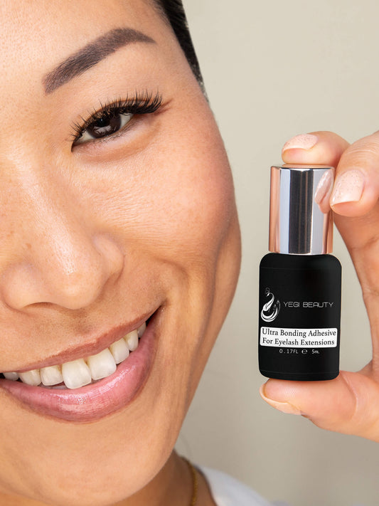 5ml black bottle with silver cap. label reads "Yegi Beauty Ultra Bonding Adhesive For Eyelash Extensions." Product being held by woman in thumb and index finger. Woman is smiling with eyelash extensions. 
