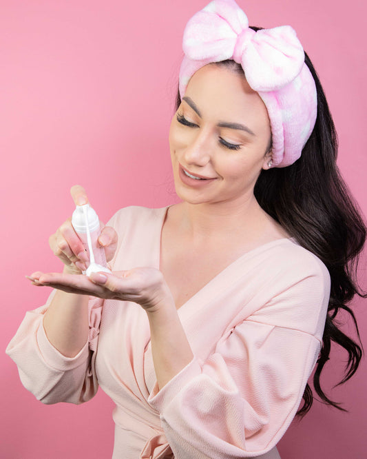 Woman in pampering attire spraying foam into hand. Woman and product shot in pink setting background. 